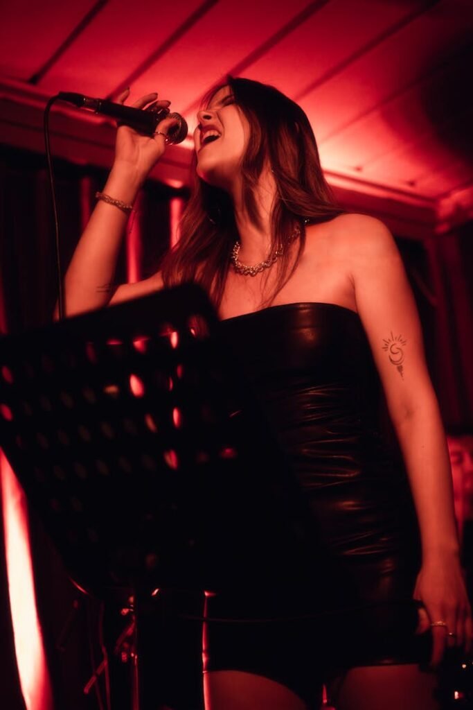 Galería Dynamic image of a woman singing on stage with ambient red lighting, capturing the energy of the performance.
