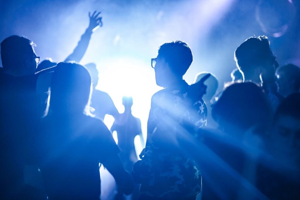 Galería Energetic scene of silhouettes dancing at a nighttime party with bright lights.