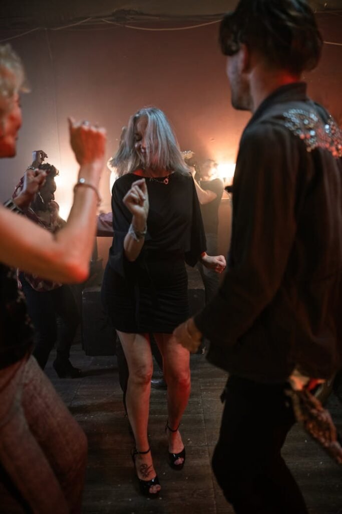 Galería A lively group of adults dancing energetically at a nightclub party under warm lights.